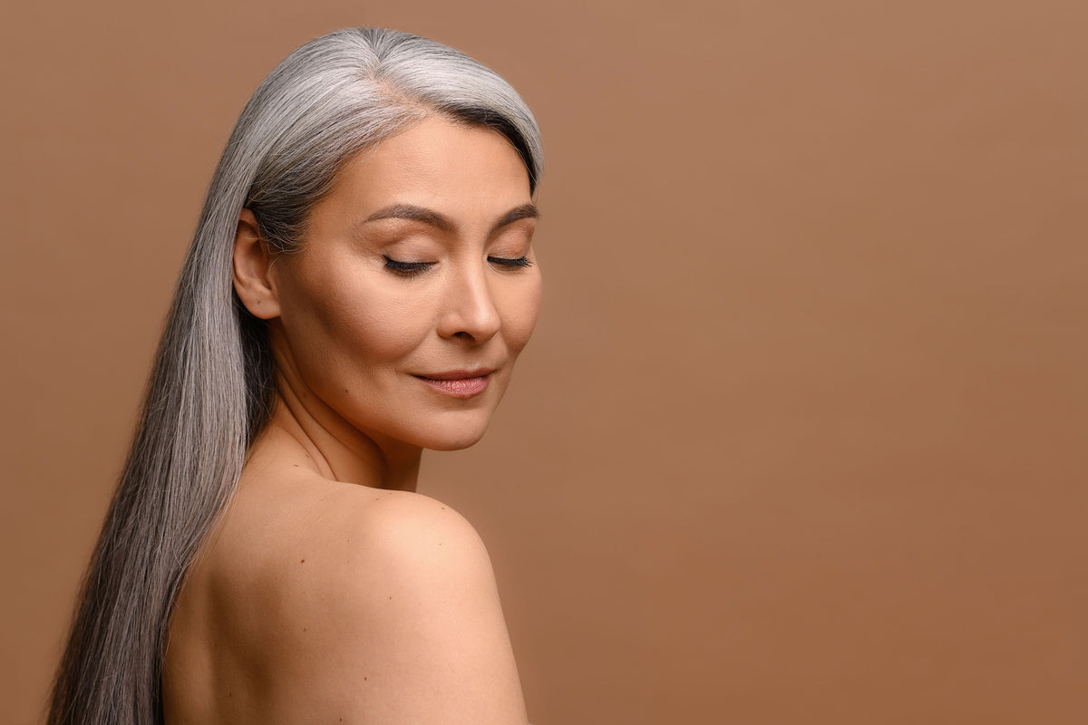 Woman with silver hair and a bare shoulder looking serenely downward in warm light