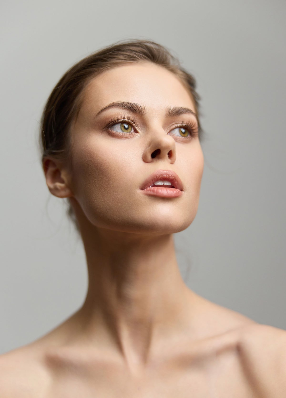Woman with bare shoulders and a clear complexion gazing upward against a grey background