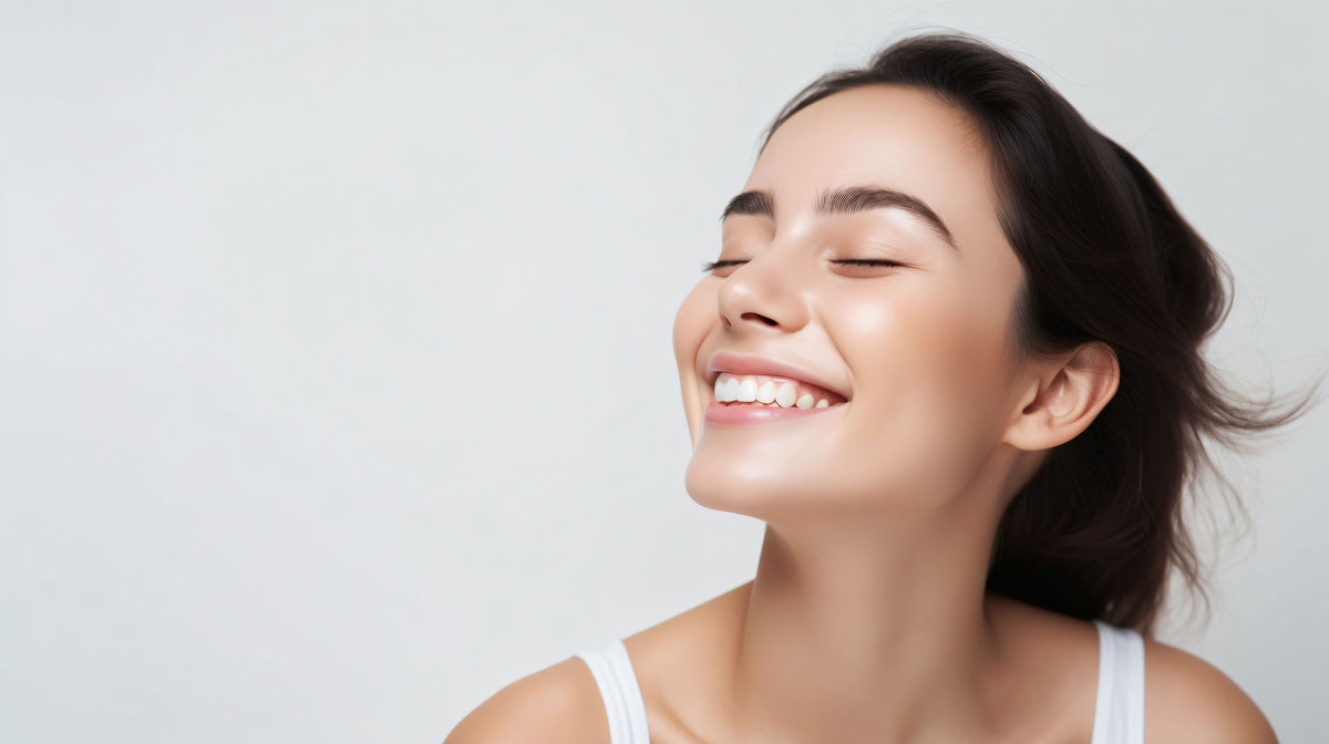 Smiling woman with eyes closed and radiant, smooth skin against a white background