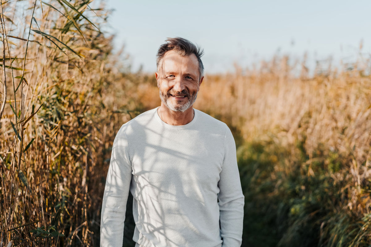 Smiling middle-aged man with grey stubble standing in a sunlit field of tall grass