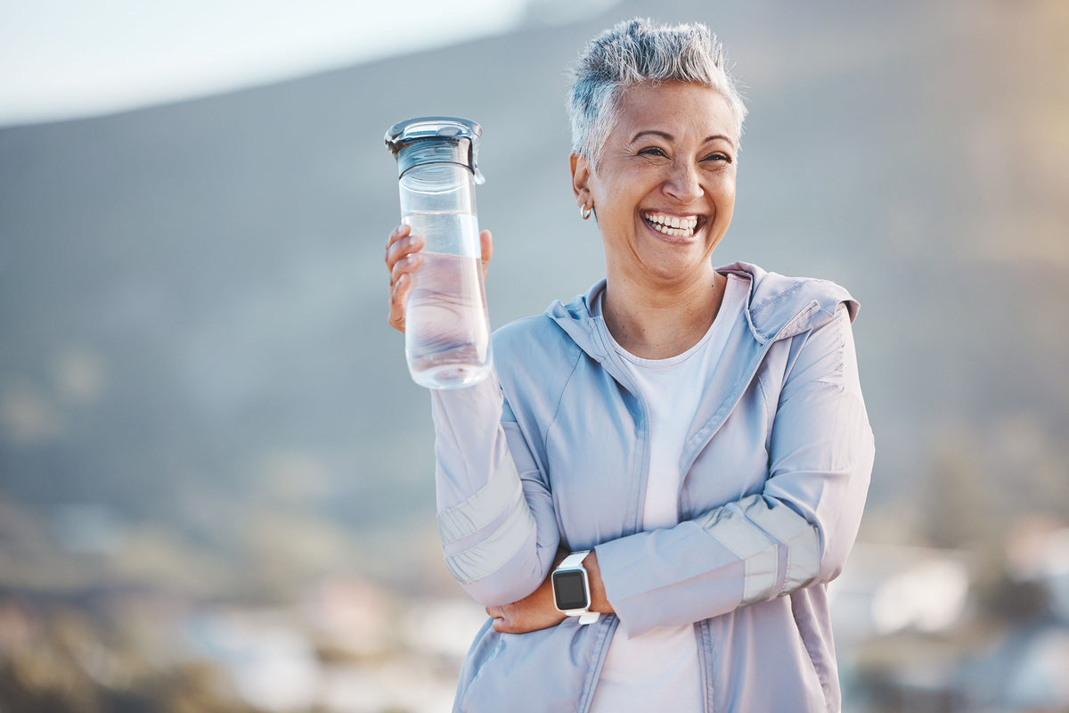 Active older woman laughing outdoors in athletic wear, holding a water bottle