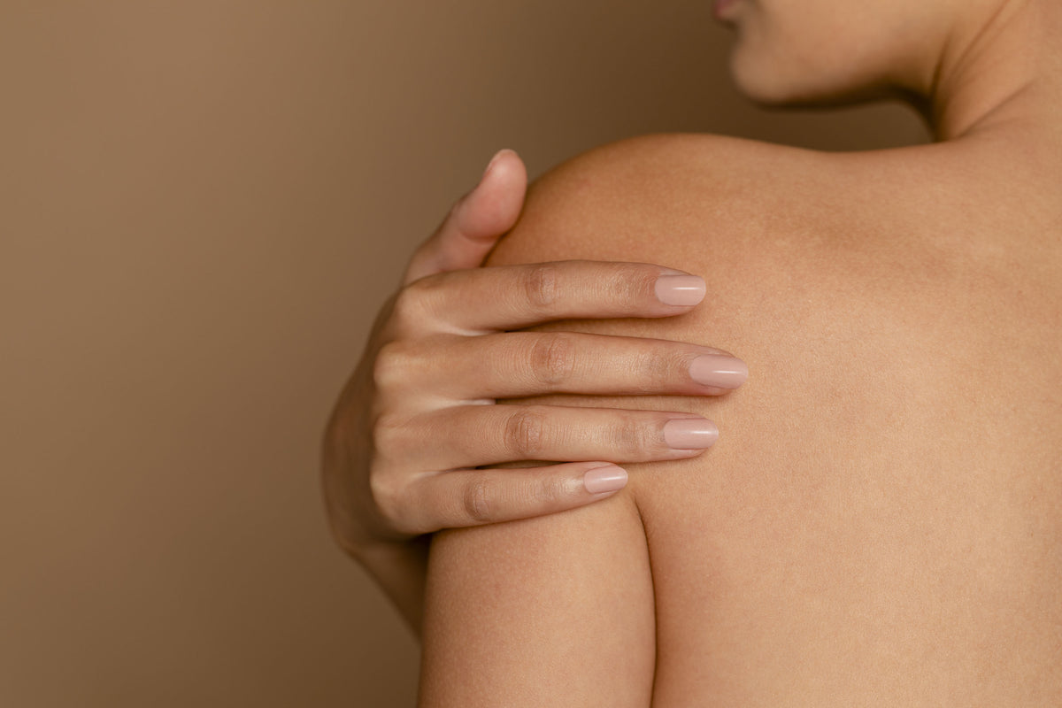 Close-up of a hand with nude nails resting on a bare, smooth shoulder