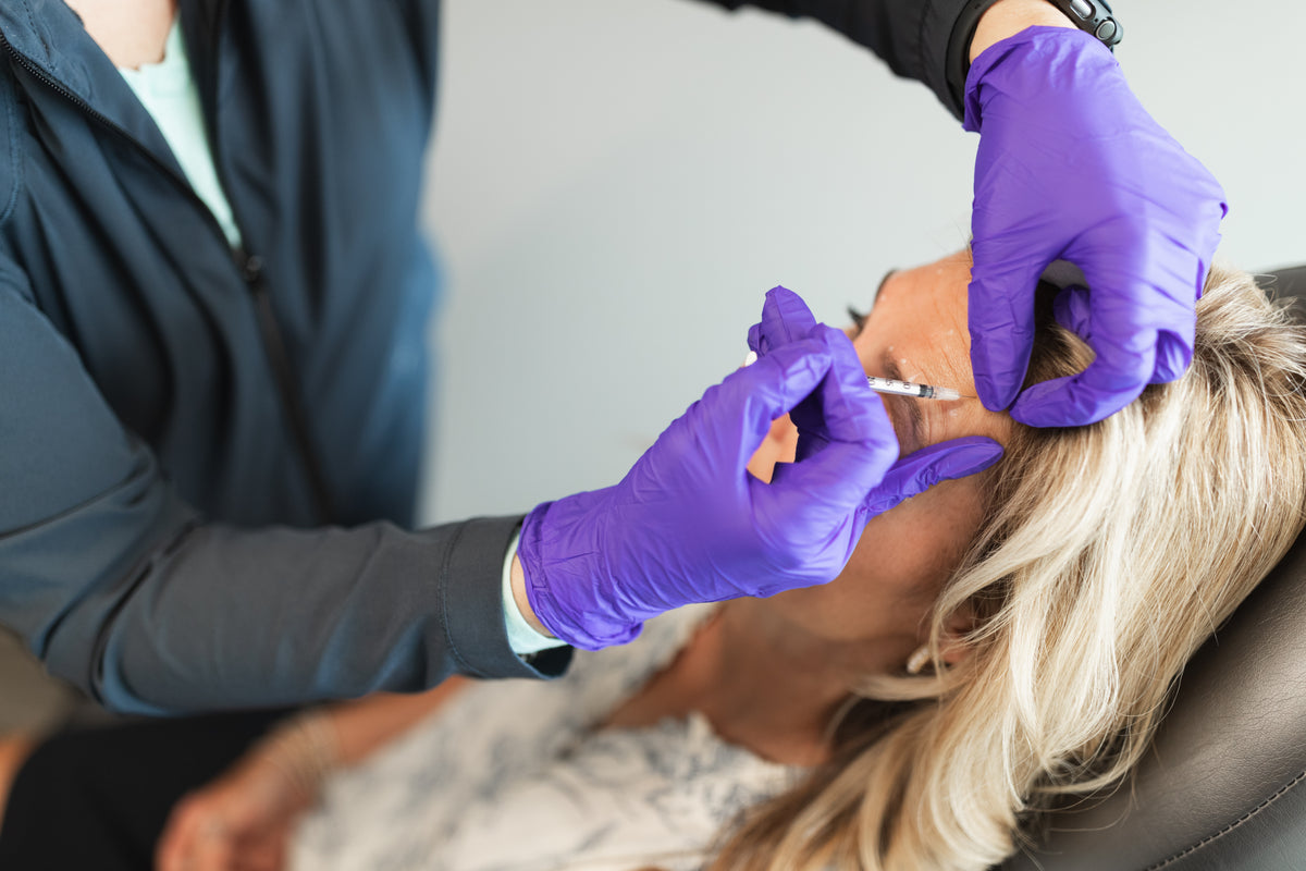 Clinician in purple gloves giving a neuromodulator injection near the brow at Element Dermatology