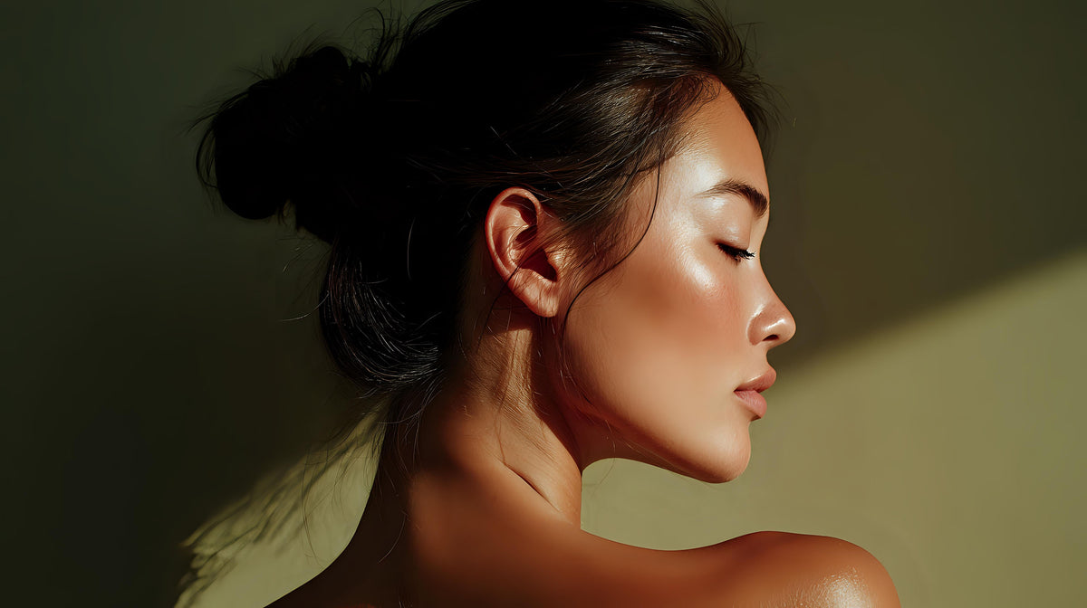 Side profile of a woman with dark hair and glowing, dewy skin in warm light