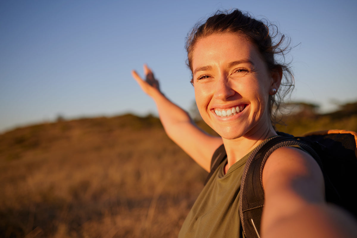 Smiling woman outdoors at golden hour with glowing skin and a clear blue sky