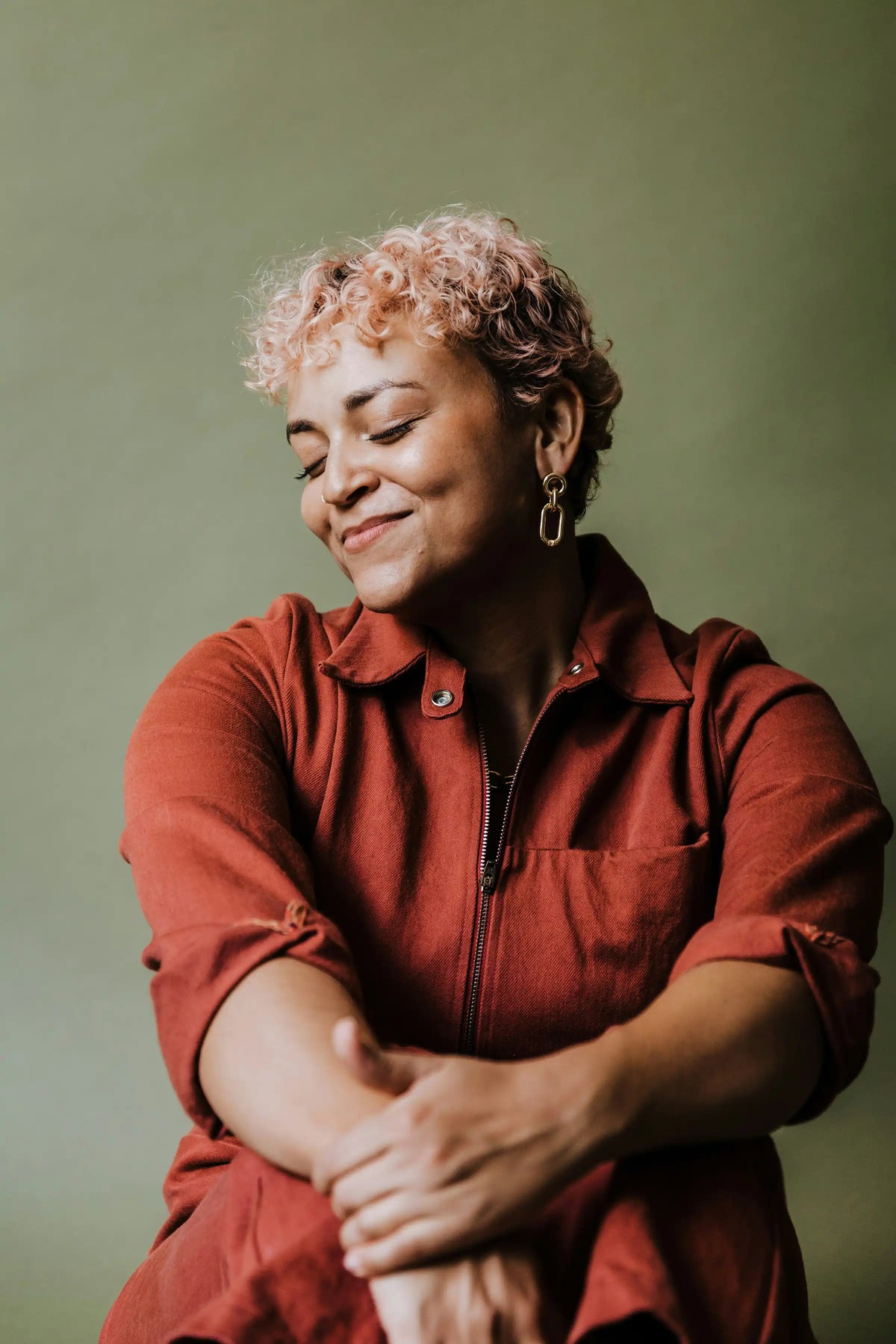 Smiling woman with short curly hair in a red top, arms folded contentedly