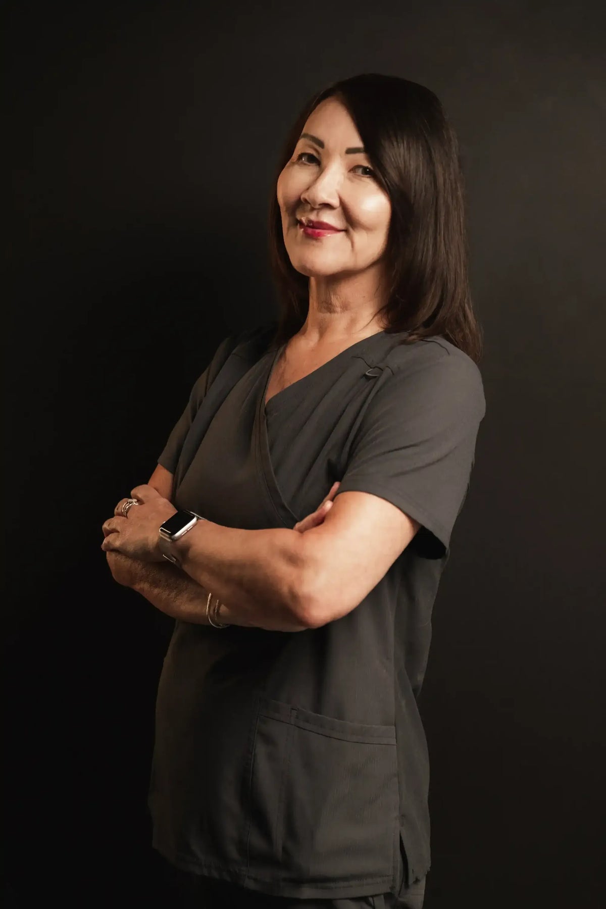 Corinne, Element Dermatology team member, with long dark hair in grey scrubs