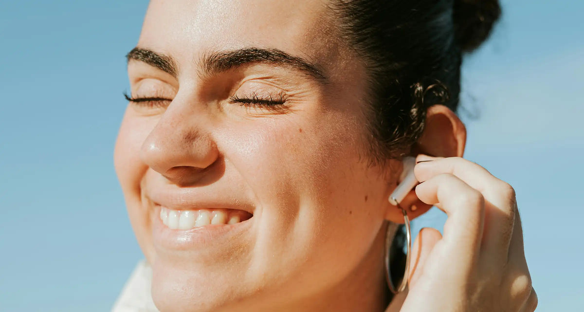 Close-up of a smiling woman with clear skin outdoors against a bright blue sky