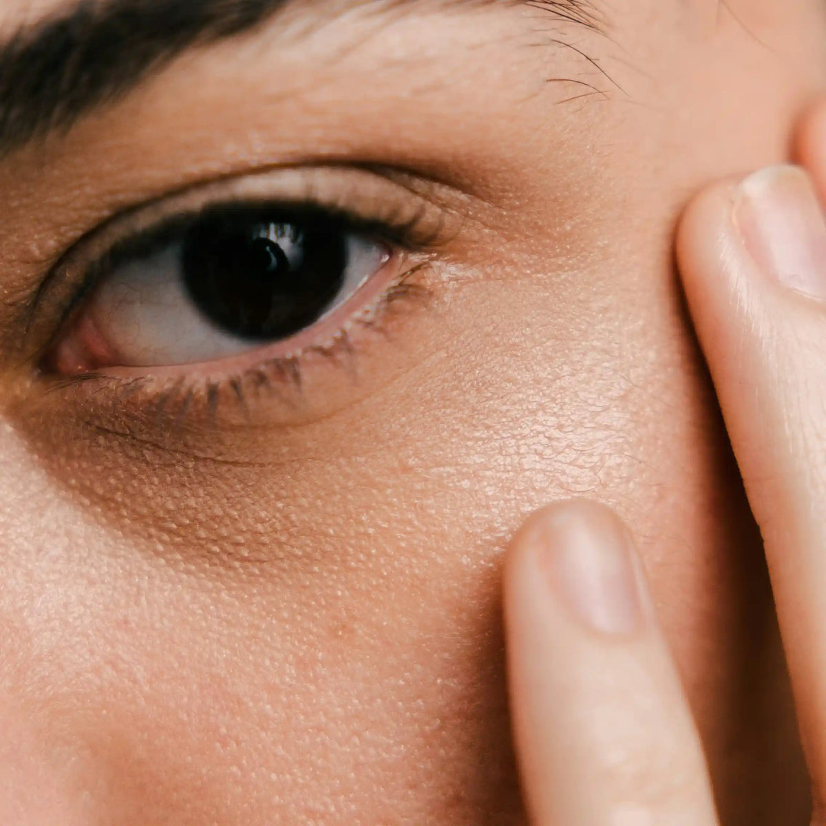 Close-up of a dark eye with fingers resting gently on the cheekbone