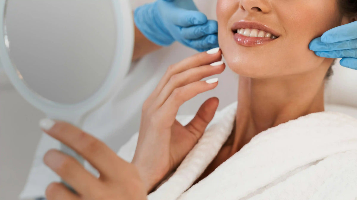 Clinician in blue gloves holding a mirror for a smiling woman in a treatment robe