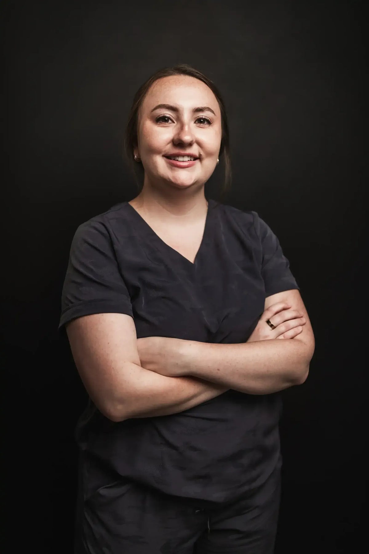 Kayla, Element Dermatology team member, with dark hair in navy scrubs, smiling