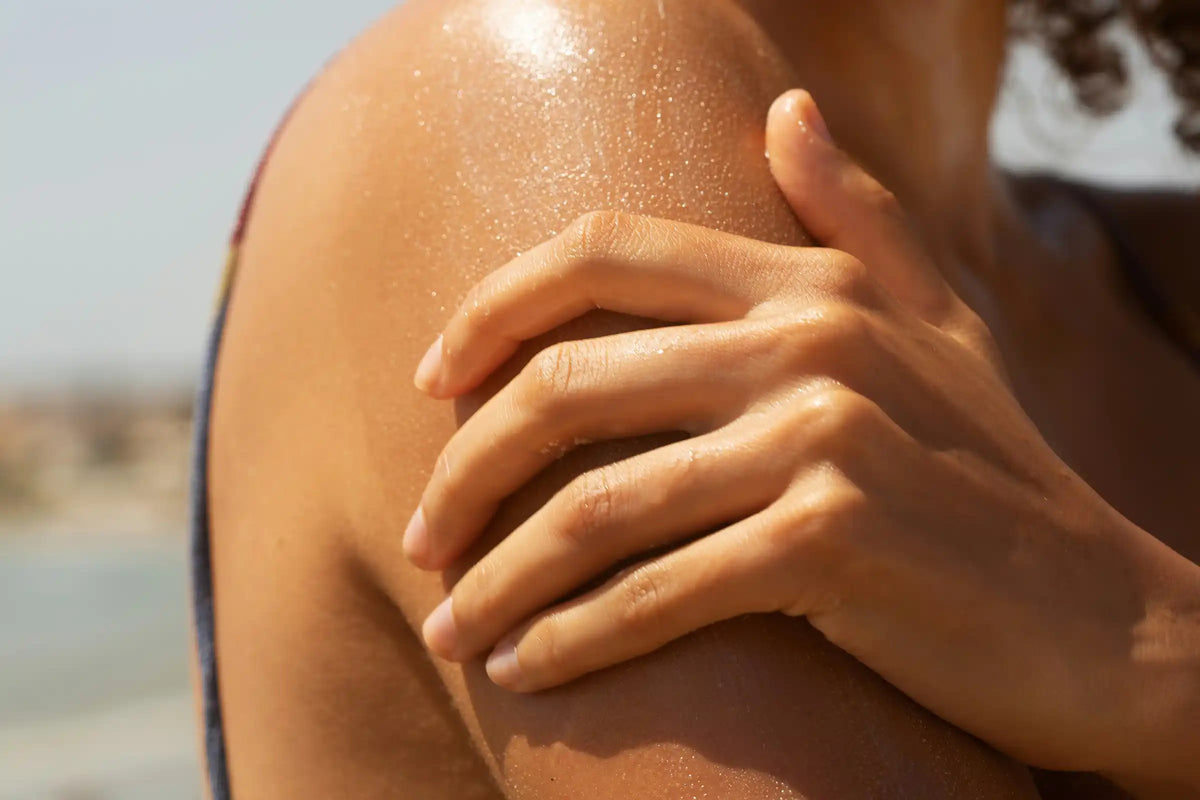 Person applying sunscreen to a sun-exposed shoulder outdoors at the beach