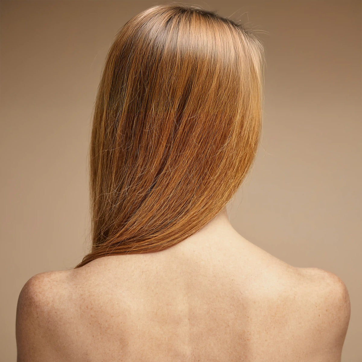Rear view of a bare-shouldered woman with auburn hair against a neutral background