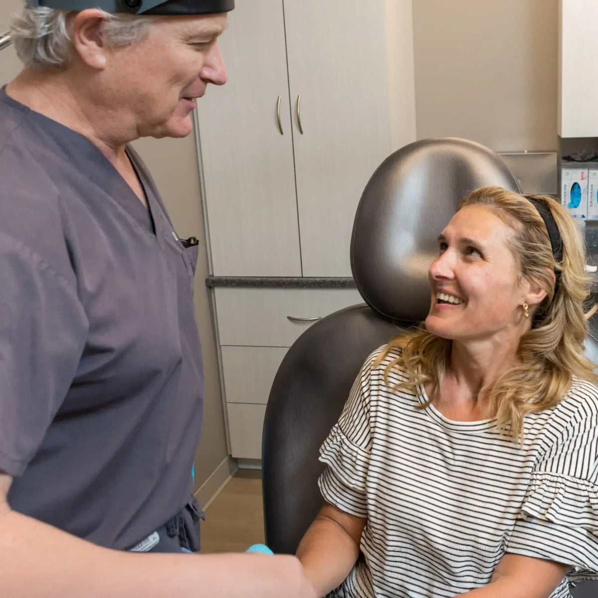 Provider in scrubs and headlamp smiling with a patient in a treatment chair at Element Dermatology