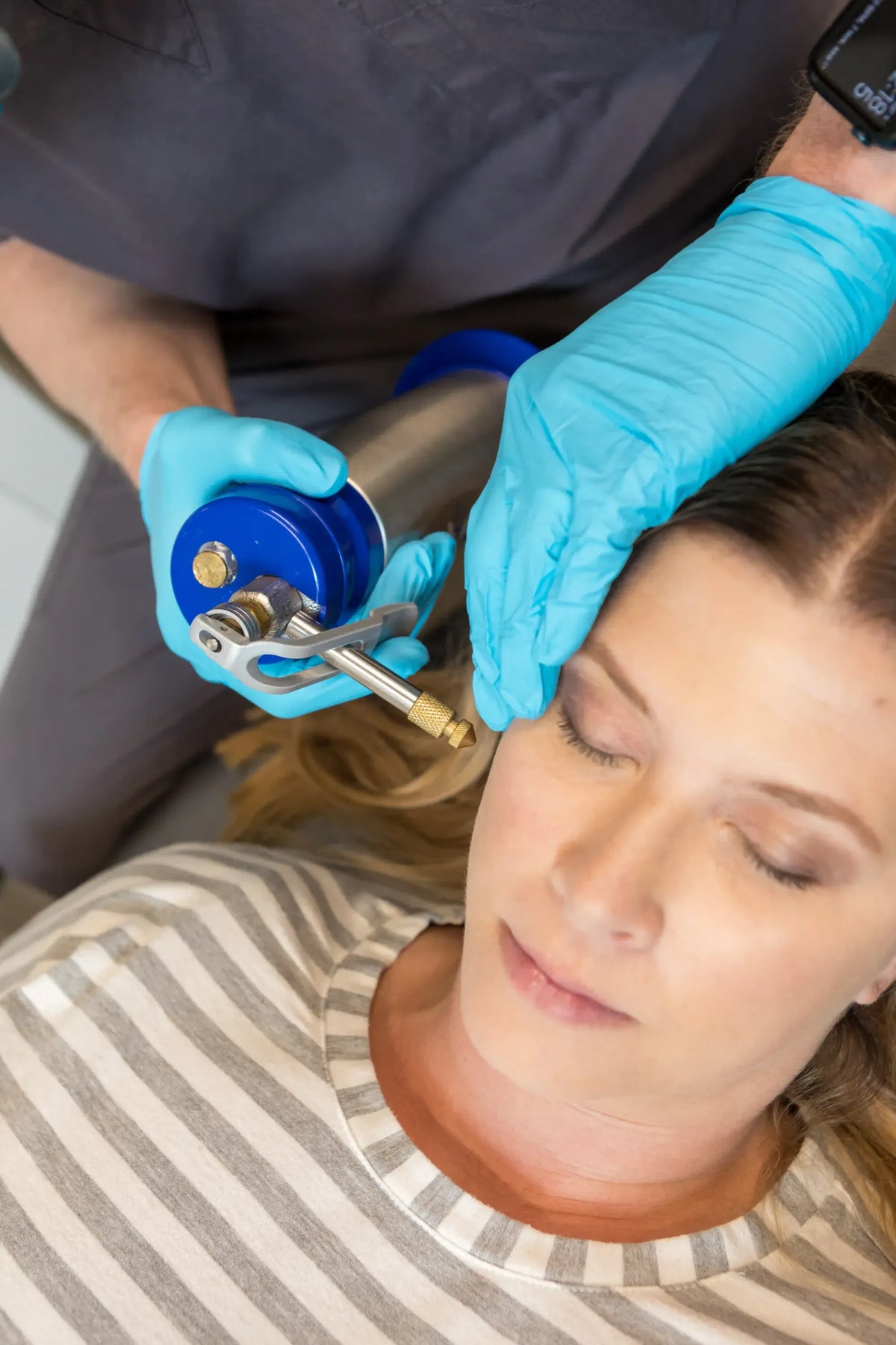 Gloved clinician holding a medical device near a reclining patient's temple at Element Dermatology
