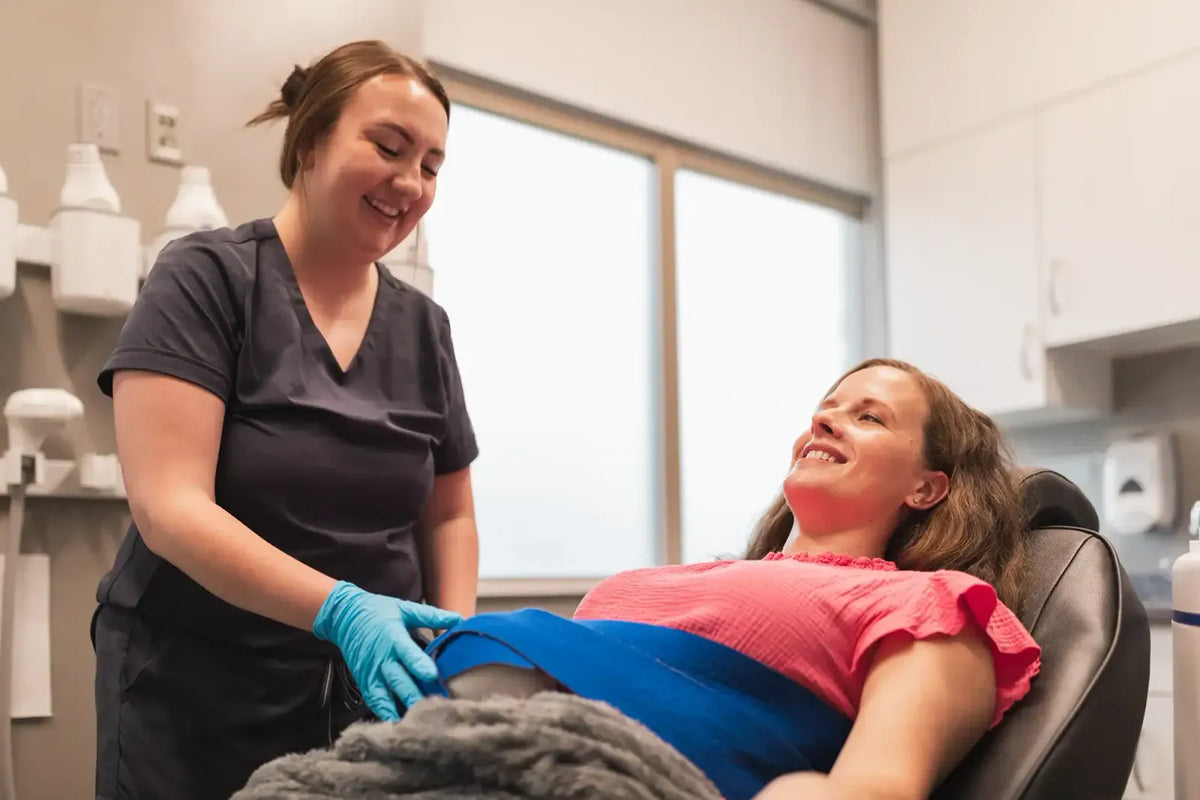 Provider in scrubs attending to a patient in a pink top in an Element Dermatology treatment room