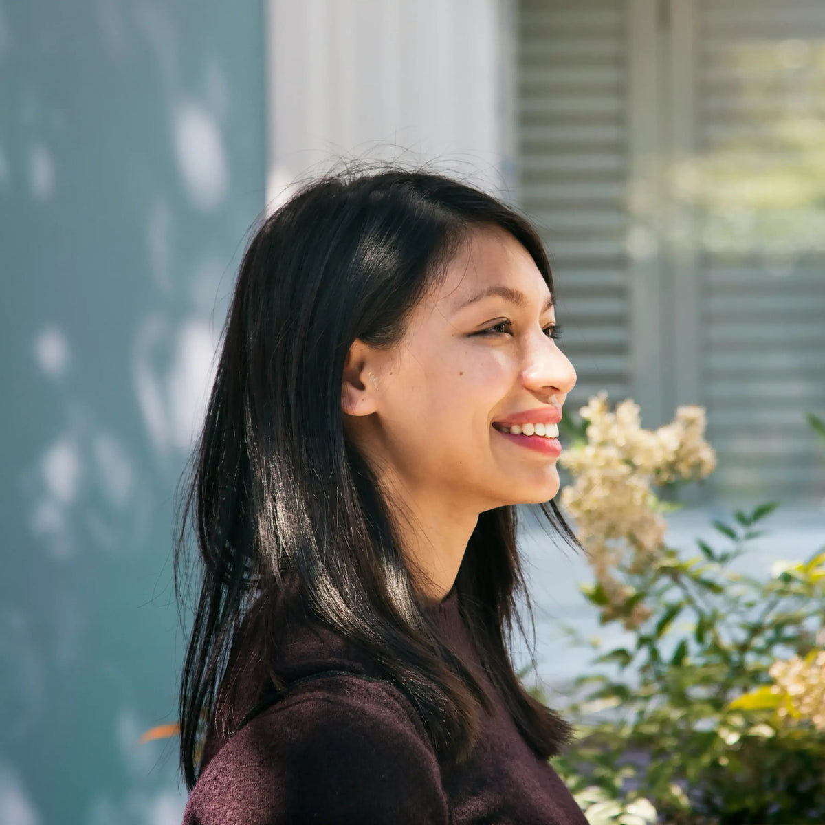 Smiling woman with long dark hair outdoors near flowering shrubs